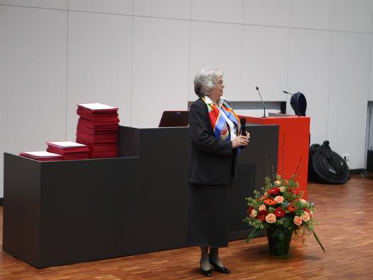 Wir sehen die Dekanin des Fachbereiches Wirtschaftswissenschaften, Prof. Dr. Felicitas Albers. Sie steht vor einem Rednerpult in einem großen Saal.